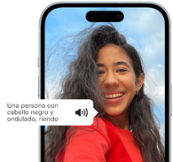 Un iPhone 15 muestra cómo la funcionalidad VoiceOver lee la descripción de una imagen: una persona con pelo negro ondulado sonriendo